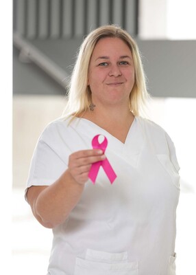Foto: Foto Muik DGKP Sarah Resner-Radakovits, Dipl. Gesundheits- und Krankenpflegerin, mit rosa Schleife in der rechten Hand